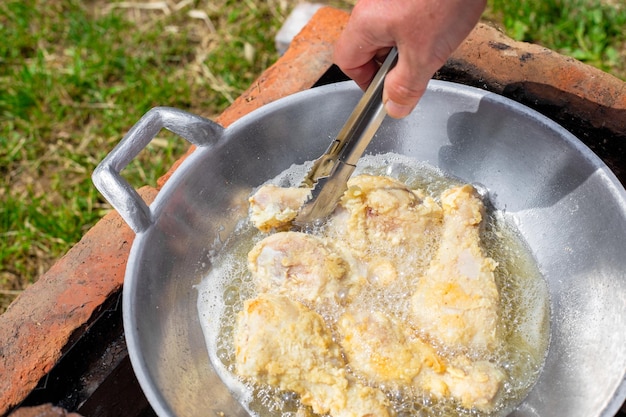 Um homem frita coxas de frango em massa em óleo em uma panela wok na dacha Cozinhando comida deliciosa em um piquenique