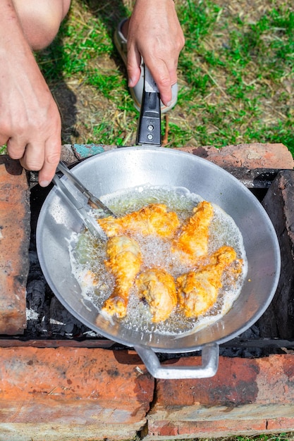 Um homem frita coxinhas de frango em óleo em uma frigideira wok Piquenique ao ar livre