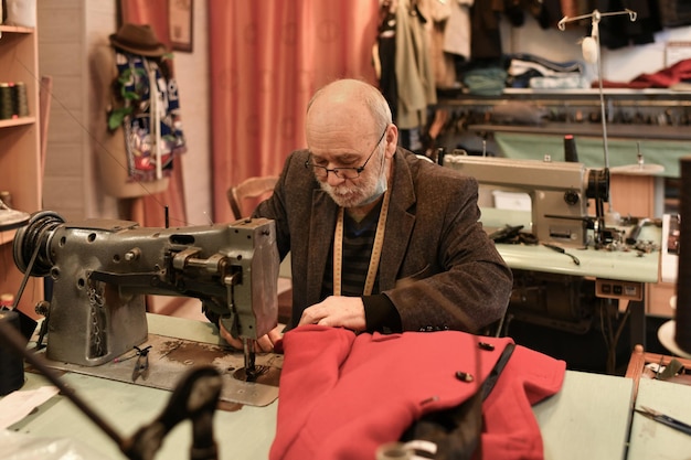 Um homem grisalho trabalha em uma máquina de costura em seu atelier