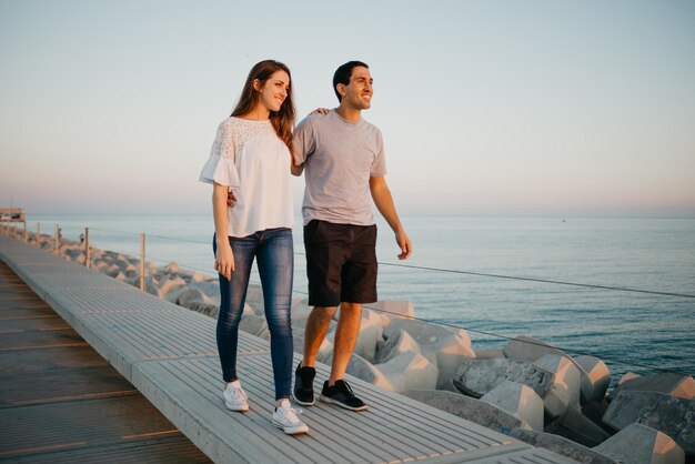 Um homem hispânico e sua namorada estão passeando em um quebra-mar na Espanha