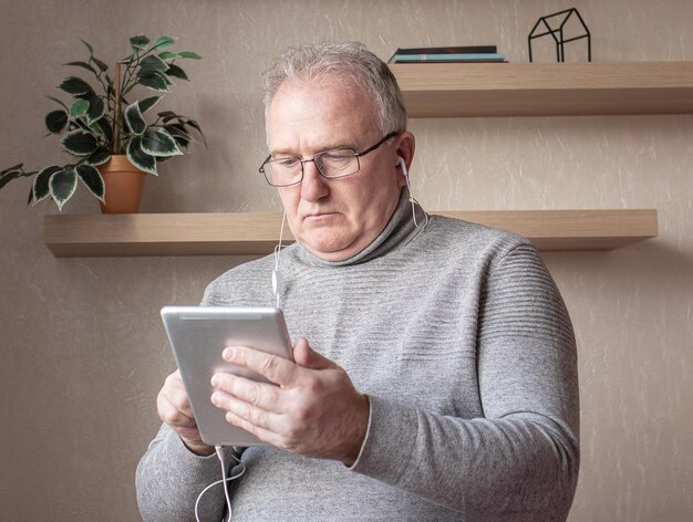 Foto um homem idoso com óculos e fones de ouvido com um tablet na mão está estudando cursos on-line conceito de ensino à distância