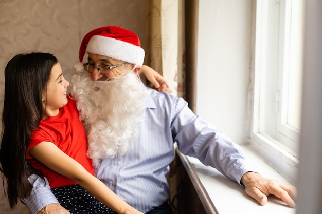 um homem idoso com um chapéu de Papai Noel e uma neta