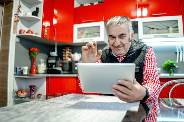 Um homem idoso com um tablet se comunica com parentes e acena com a mão.