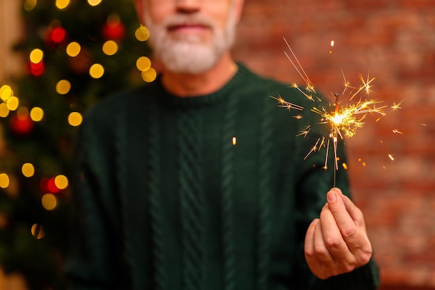 Um homem idoso de malha verde com estrelinha perto da árvore de natal