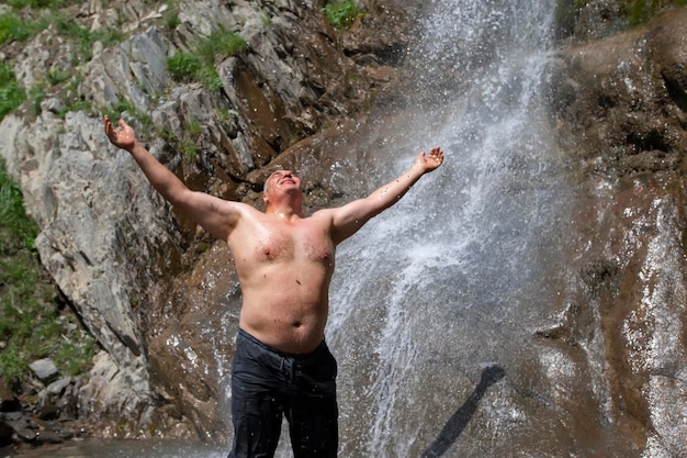 Um homem idoso fica em uma cachoeira de montanha abre os braços e aproveita o momento