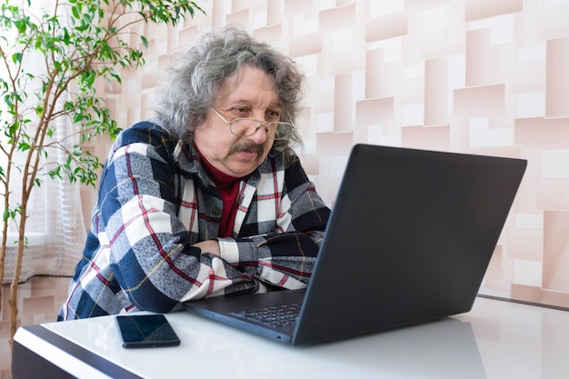 Um homem idoso se senta em uma mesa e assiste a um vídeo em um computador Homem sênior trabalhando em um laptop