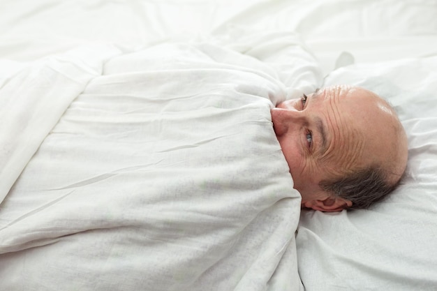 Um homem idoso tem medo do escuro e se esconde debaixo de um cobertor Problemas para dormir na velhice