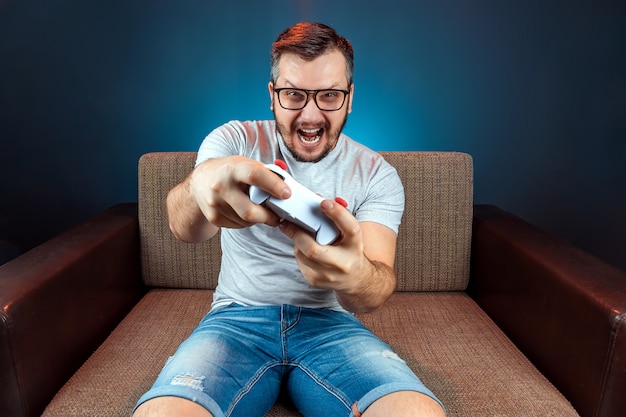 Um homem joga um console de videogame enquanto está sentado em um sofá. dia de folga, entretenimento, lazer.