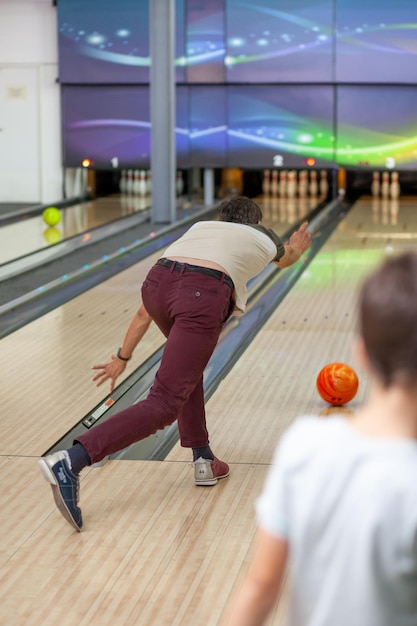 Um homem joga uma bola em uma pista de boliche. Caminhos com bolas e pinos para boliche. Um jogo divertido