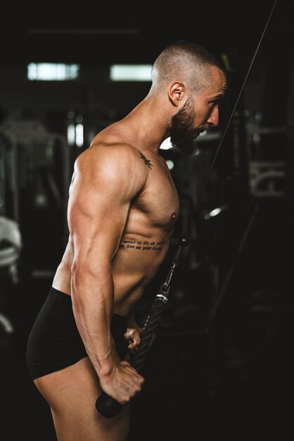 Um homem jovem fisiculturista muscular fazendo treinamento duro para os músculos dos braços no ginásio.