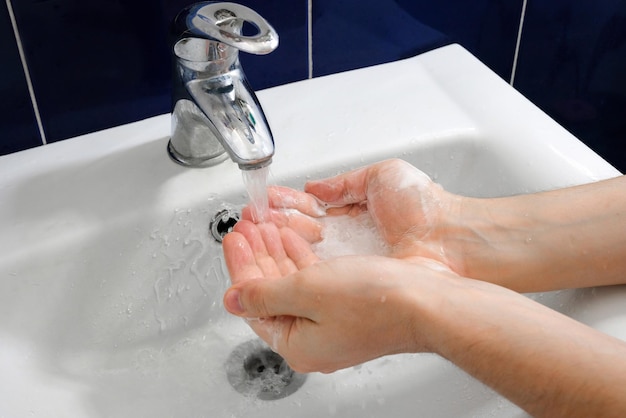 Um homem lava as mãos com sabão sobre uma pia branca no conceito de higiene do banheiro
