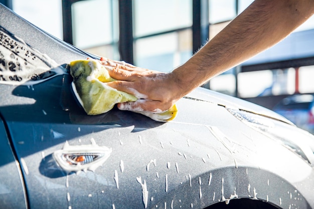 Um homem lava seu carro com espuma em uma lavagem de carros self-service fechada