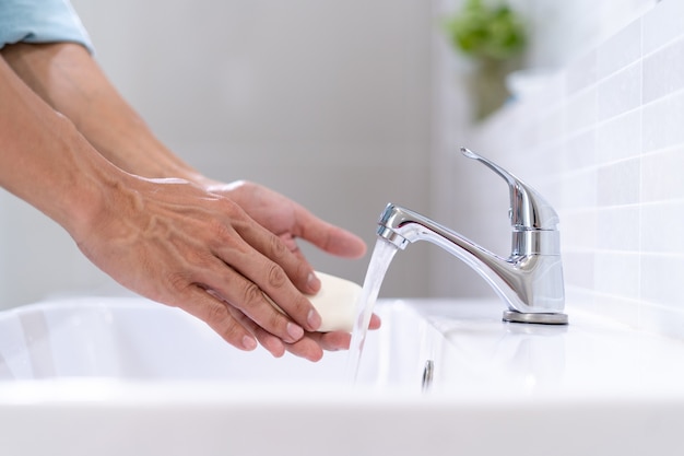 Um homem lavando as mãos com sabão e água limpa em uma pia. prevenir a propagação do vírus corona lavando as mãos com frequência.