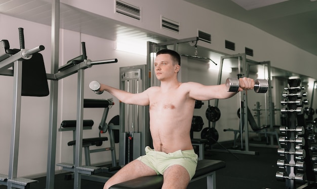 Um homem levanta halteres na sala de ginástica. um homem pratica esportes em um centro esportivo. uma pessoa se preocupa com sua saúde. torso nu