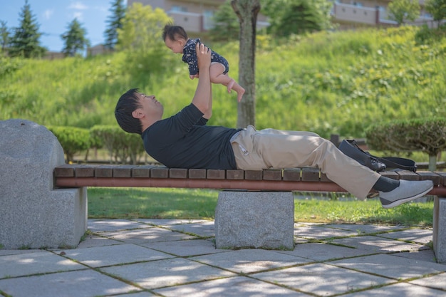 Um homem levanta um bebê em um banco de um parque.