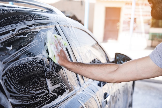 Um homem limpa a espuma do carro com um pano. lava-jato