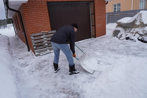 Um homem limpa a neve no inverno no pátio da casa