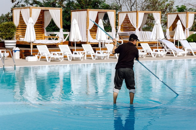 Um homem limpa a piscina Homem limpando a piscina com aspirador de pó