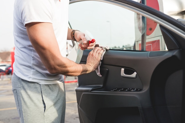 Um homem limpando o carro com pano de microfibra, conceito de detalhamento (ou manutenção) do carro. Foco seletivo na mão do homem.