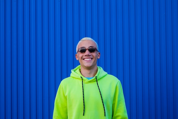 Um homem louco e feliz usando óculos elegantes, sorrindo e se divertindo olhando para a câmera, curtindo - um suéter colorido com uma parede azul ao fundo