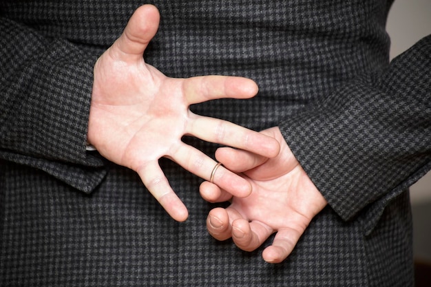 Um homem lutando para remover o anel de casamento do dedo segurando as mãos atrás das costas