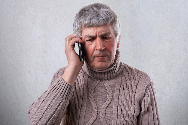 Um homem maduro com raiva, com cabelos grisalhos e rugas, segurando o smartphone na mão, comunicando-se com seus filhos