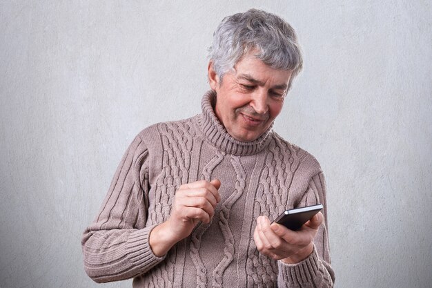 Foto um homem maduro sorridente feliz segurando seu smartphone nas mãos, sendo o prazer de receber a mensagem de seu filho