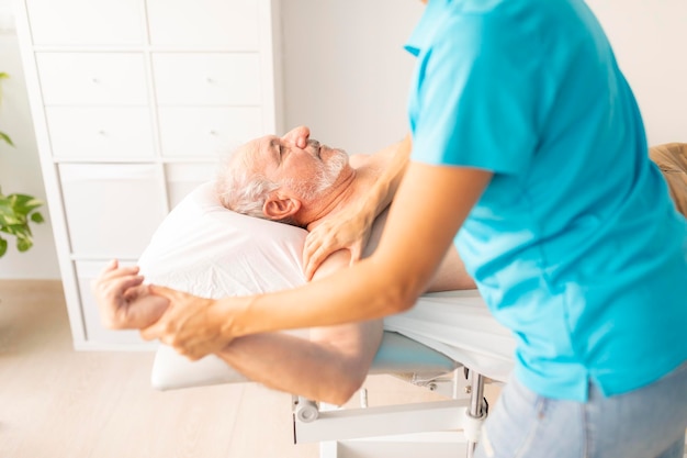 Um homem mais velho deitado na mesa em uma clínica de fisioterapia durante uma sessão de terapia manual
