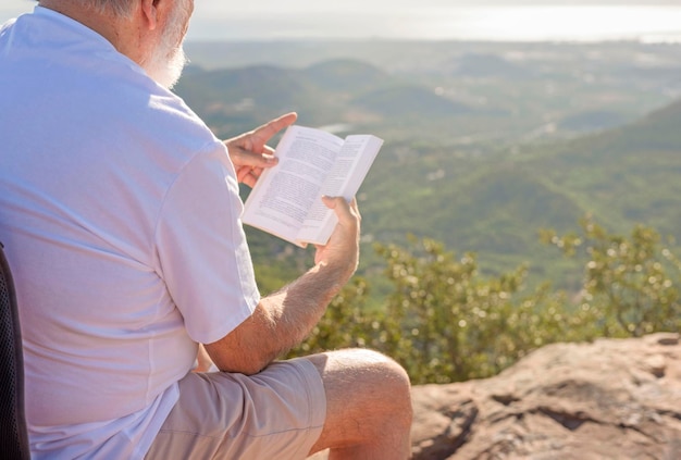 Um homem mais velho irreconhecível sentado na montanha lendo um livro