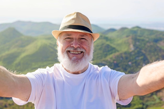 Um homem mais velho tirando uma selfie no topo da montanha