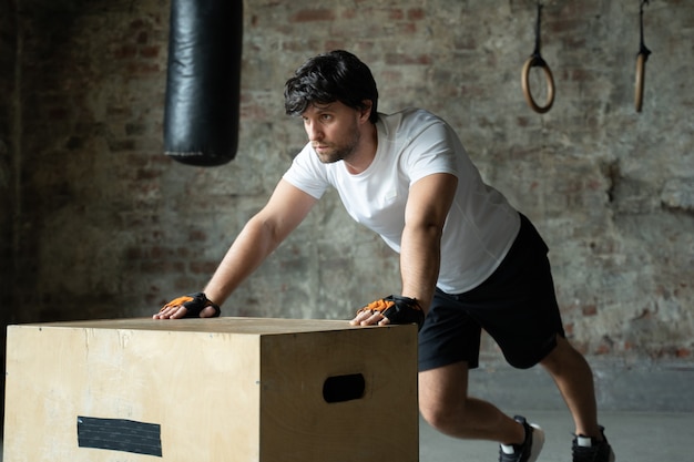Um homem malhando na academia faz flexões em uma caixa de madeira