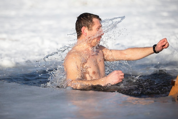 Um homem mergulha em um buraco no gelo durante o festival de inverno do batismo de jesus. um homem nada no buraco de gelo no inverno. pessoas da morsa.