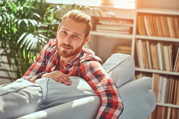 Um homem modelo jovem ruiva bonito senta-se em um sofá na sala com um interior loft.