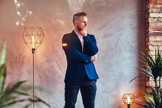 Um homem moderno e elegante, vestido com um terno elegante, posando em uma sala com interior loft.