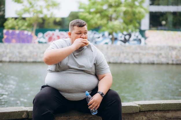 Um homem muito gordo está a comer um hambúrguer.