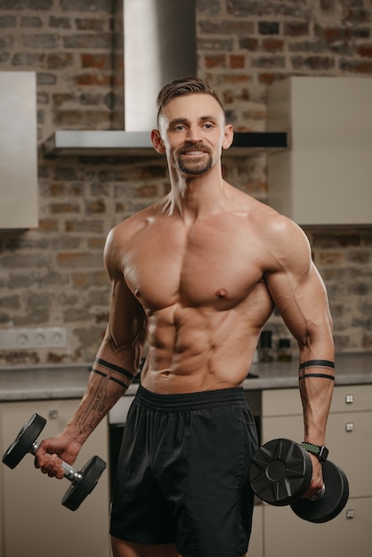 Um homem musculoso com barba posando com halteres em seu apartamento