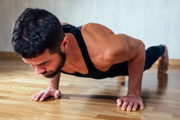 Um homem musculoso faz exercícios para fortalecer os músculos das mãos na flexão do chão do conceito de promoção da saúde e corpo bonito