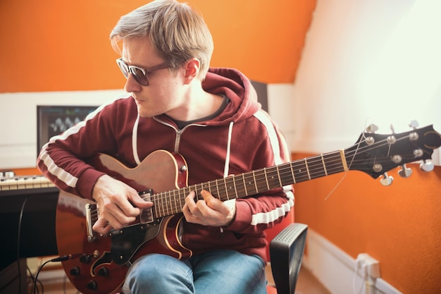 Um homem músico de óculos tocando violão e gravando uma música no estúdio