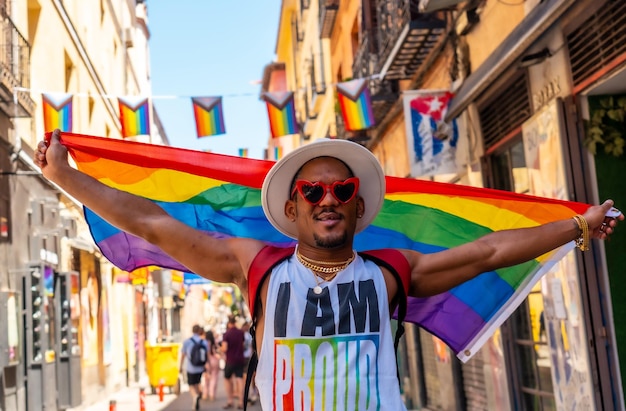 Um homem negro gay curtindo e sorrindo na festa do orgulho com uma bandeira LGBT