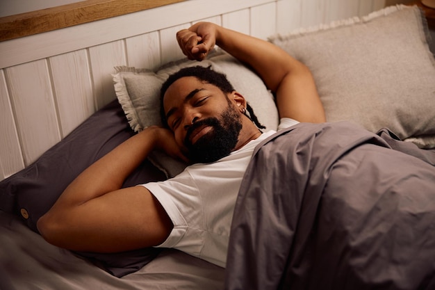 Um homem negro sorridente a esticar-se na cama de manhã.