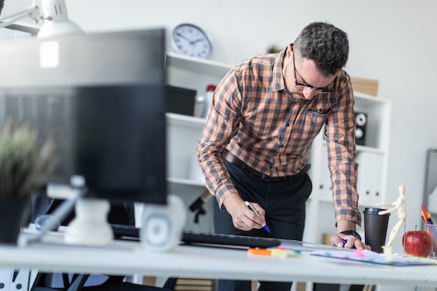 Um homem no escritório está parado perto da mesa e desenha um marcador no quadro magnético.