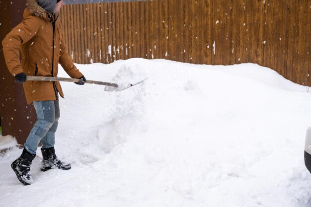 Um homem no inverno limpa a neve com uma pá no quintal de uma casa no estacionamento Queda de neve condições climáticas difíceis o carro está parando desenterrando a passagem