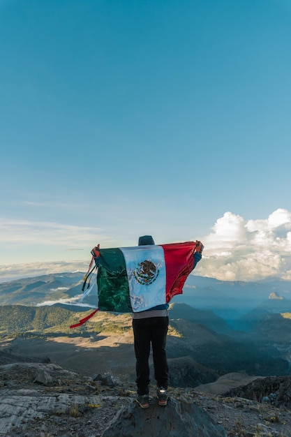 Um homem no topo da montanha com a bandeira mexicana