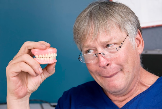 Foto um homem olha para sua dentadura antes de colocá-la de volta na boca
