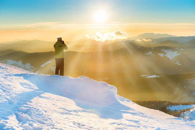 Um homem olhando para o sol e o belo pôr do sol nas montanhas de inverno com neve