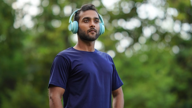 Um homem parado no parque com fones de ouvido no ouvido