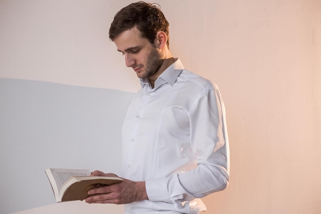 Foto um homem parado perto da parede branca folheando um livro