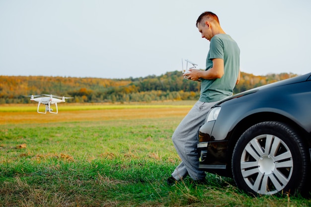 Um homem parado perto do carro lança um drone. voo do drone em campo amarelo