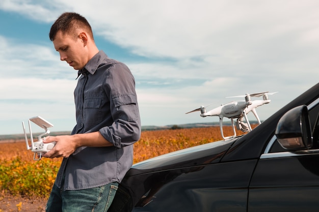 Um homem parado perto do carro lança um drone. voo do drone em campo amarelo