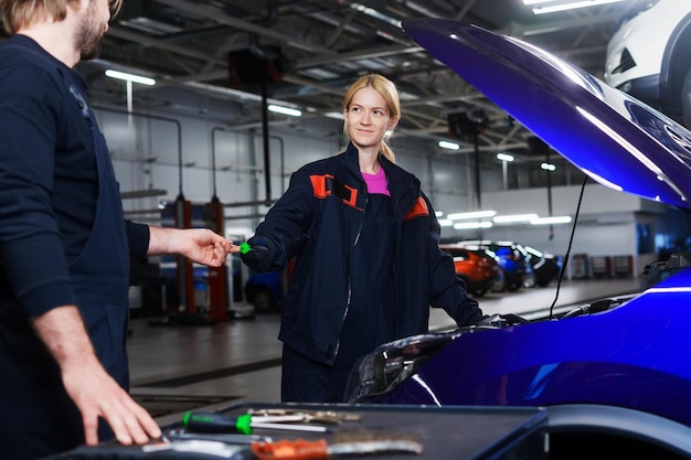 Um homem passa uma chave de fenda a um colega de uma jovem para reparar um carro Estação profissional de reparo e diagnóstico de carros